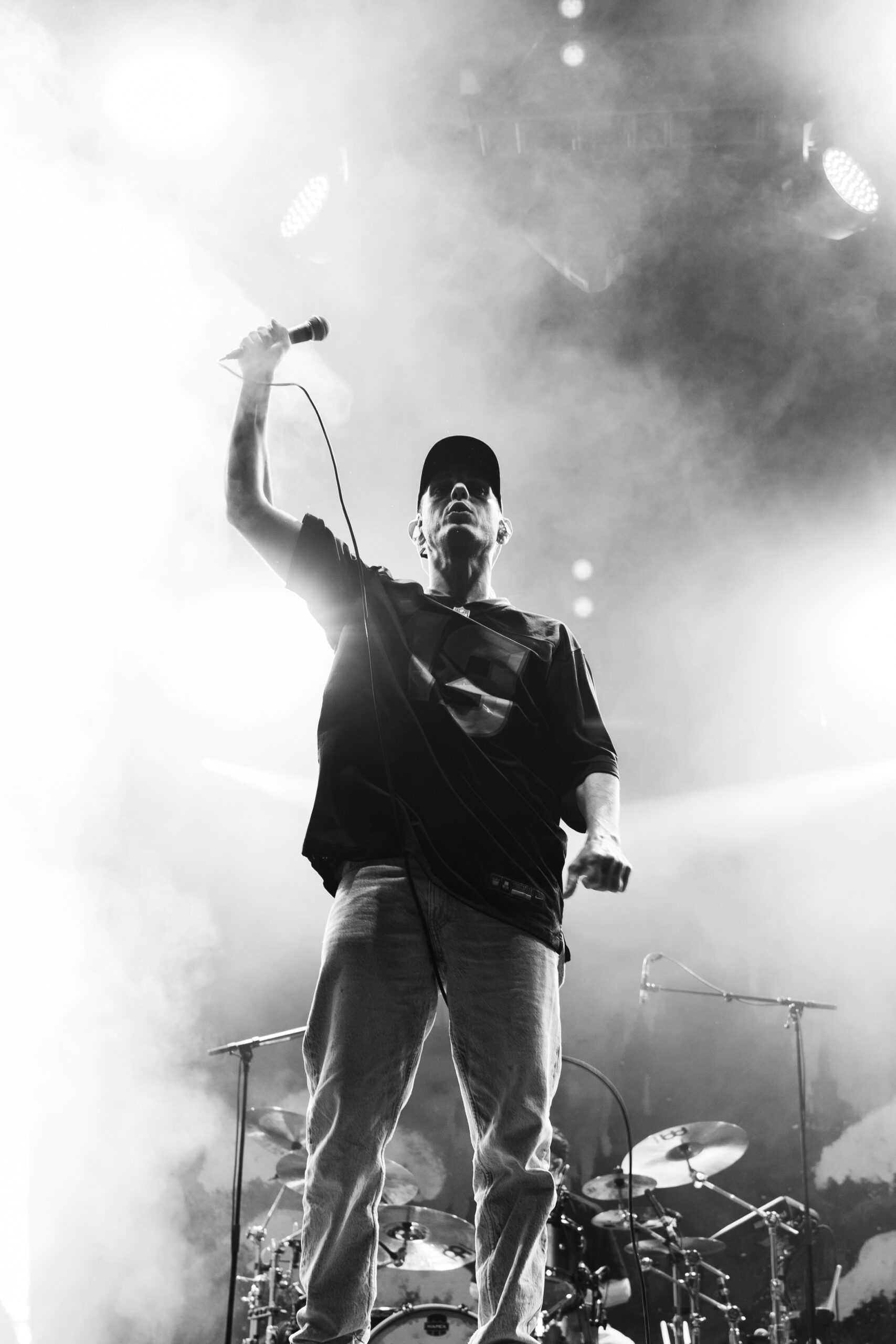 Chanteur micro levé en contre-plongée sous la fumée — photo concert N&B Greg Raw